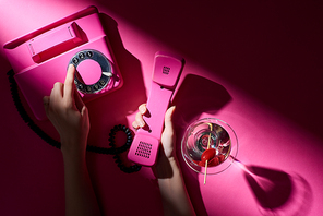 Cropped view of woman using vintage telephone beside cocktail on pink background