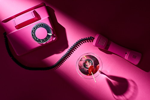 Top view of vintage telephone and cocktail with shadow on pink background