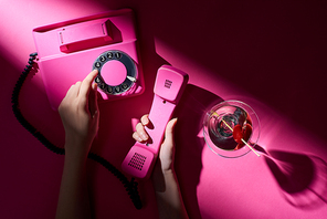 Cropped view of woman using retro telephone with martini beside on pink background