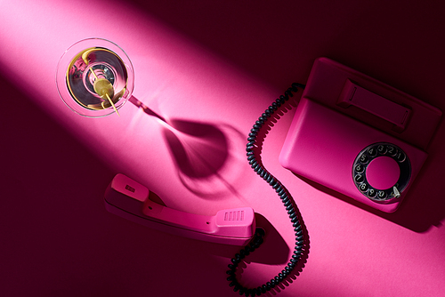 Top view of martini and retro telephone on bright pink background