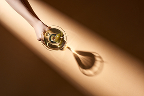 Cropped view of woman holding glass of martini on beige background