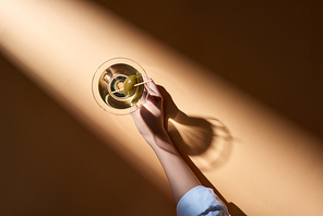 Cropped view of woman holding martini on beige background with shadow