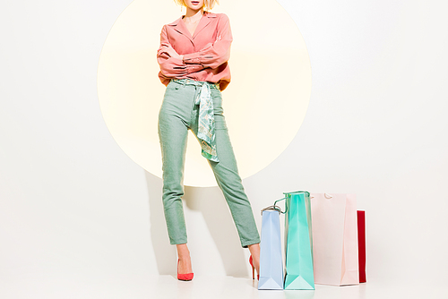 cropped view of stylish girl with arms crossed posing near shopping bags on white with yellow circle