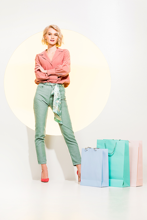 beautiful stylish girl with arms crossed posing near shopping bags on white with yellow circle