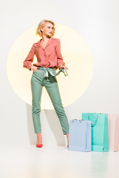 beautiful fashionable girl posing near shopping bags on white with yellow circle