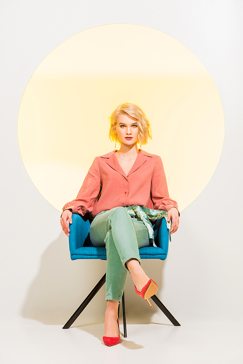 beautiful stylish girl in colorful clothes  and sitting in armchair on white with yellow circle