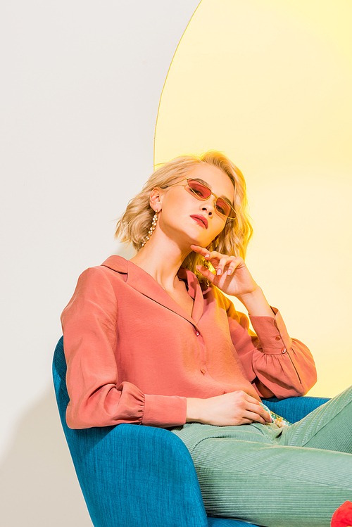 beautiful stylish blonde girl in colorful clothes  and sitting in armchair on white with yellow circle