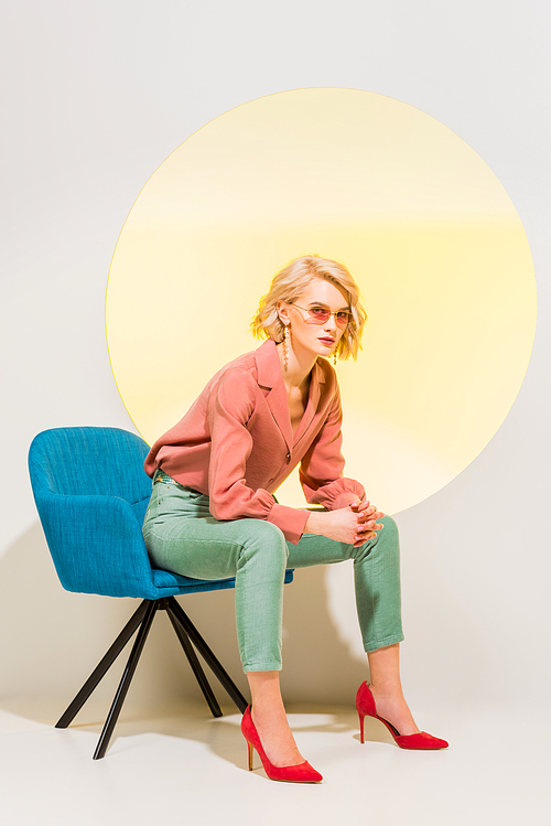 beautiful fashionable girl in colorful clothes sitting in armchair on white with yellow circle