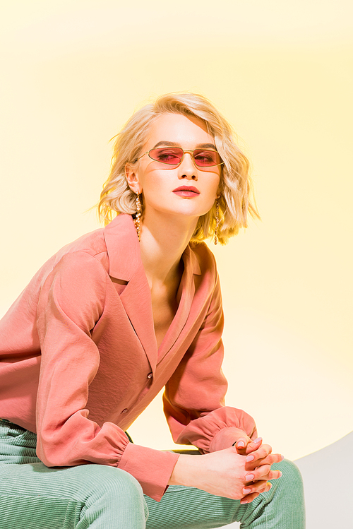 beautiful stylish girl in coral jacket and sunglasses posing on yellow