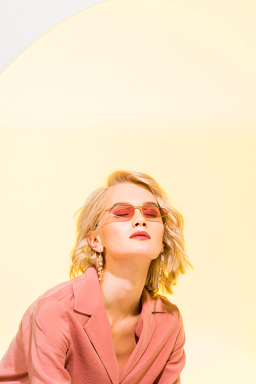 beautiful stylish blonde girl in coral jacket posing on yellow with copy space
