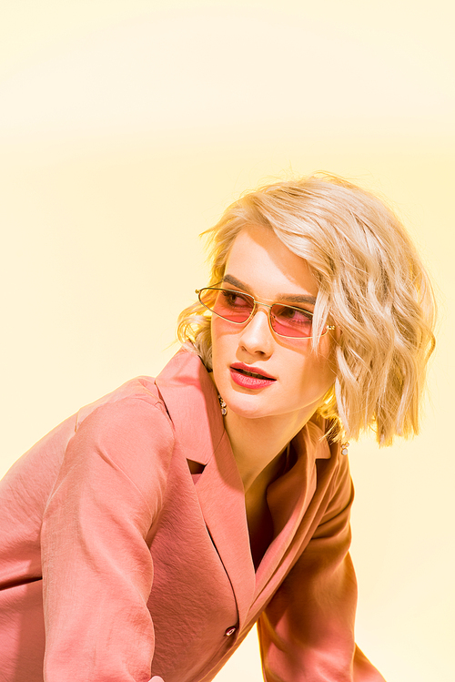 beautiful stylish girl in coral jacket and sunglasses posing on yellow with copy space