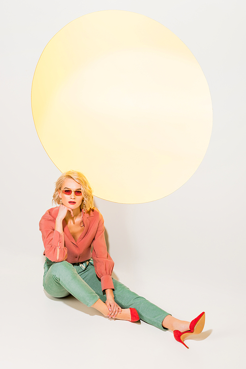 beautiful stylish girl in colorful clothes and sunglasses posing on white with yellow circle