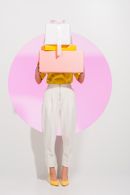 stylish girl covering face with gift boxes on white with pink circle