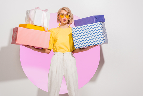 surprised stylish girl holding gift boxes and  on white with pink circle