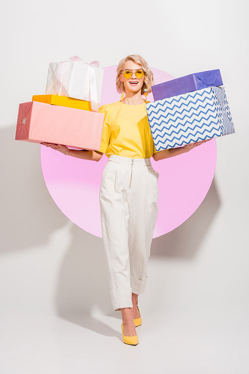 beautiful stylish girl holding gift boxes and smiling on white with pink circle