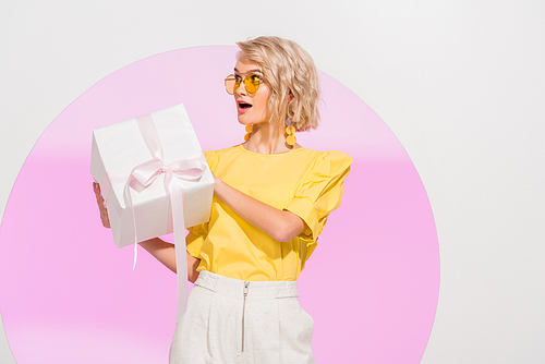 excited stylish girl holding gift box on white with pink circle