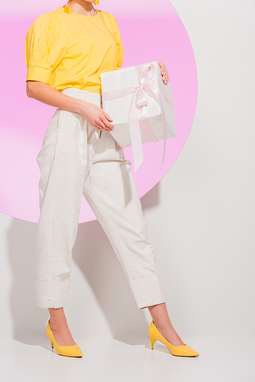 cropped view of stylish girl holding gift box on white with pink circle