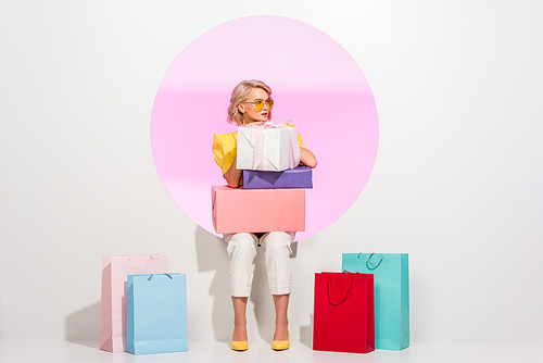 beautiful stylish girl posing with colorful gift boxes and shopping bags on white with pink circle