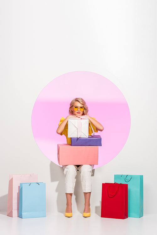 beautiful stylish girl posing with colorful gift boxes and shopping bags on white with pink circle