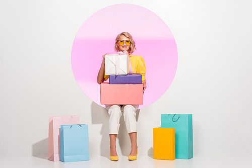 beautiful fashionable girl posing with colorful gift boxes and shopping bags on white with pink circle