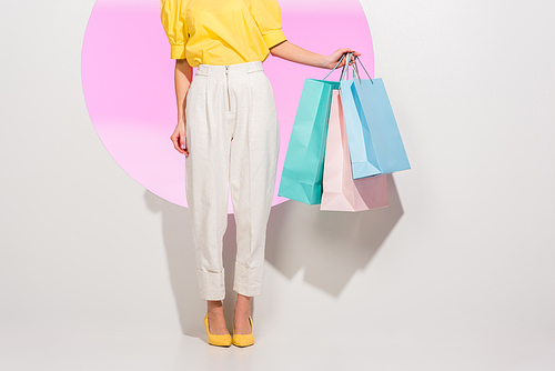 partial view of stylish girl holding colorful shopping bags on white with pink circle