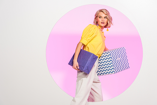 beautiful stylish young woman holding gift boxes and posing on white with pink circle and copy space