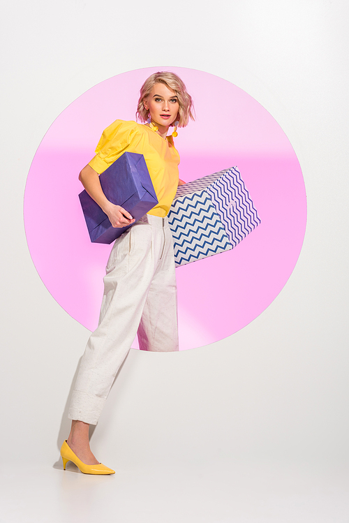 beautiful fashionable girl holding gift boxes,  and posing on white with pink circle