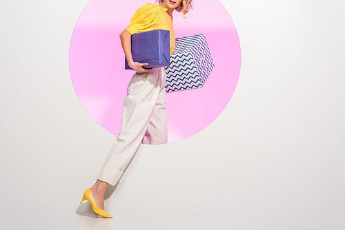 cropped view of stylish young woman holding gift boxes on white with pink circle and copy space