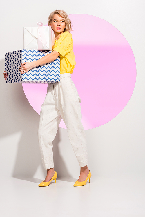 beautiful fashionable girl holding gift boxes and posing on white with pink circle