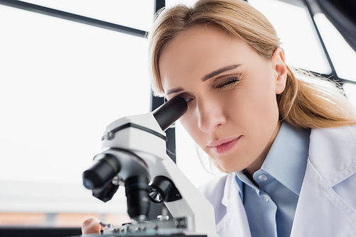 scientist looking through microscope on blurred foreground