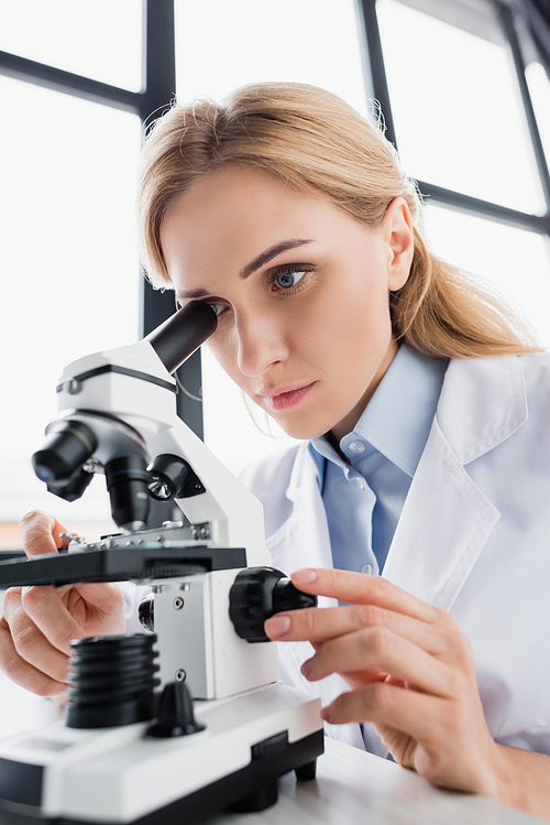 attractive scientist looking through microscope on blurred foreground