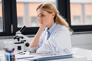 sad scientist leaning on hand near microscope in lab