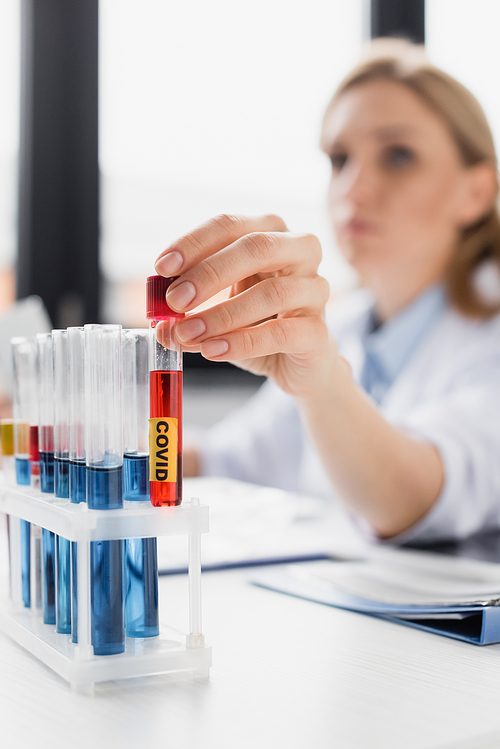 test tube with sample and covid lettering in hand of nurse on blurred background
