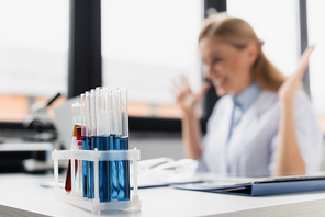 test tubes with samples near cheerful scientist on blurred background
