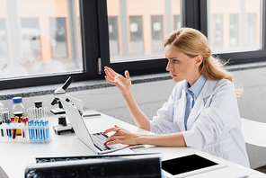 displeased scientist gesturing near laptop and microscope in lab
