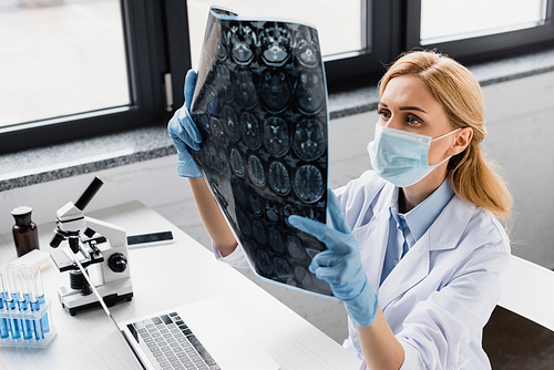 scientist in medical mask looking at x-ray near devices and microscope on desk