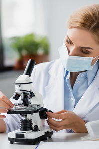 female scientist in medical mask using microscope in lab