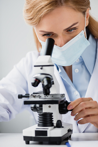 female scientist in medical mask looking through microscope in laboratory