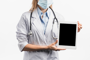 cropped view of nurse in medical mask and white coat holding digital tablet with blank screen isolated on white