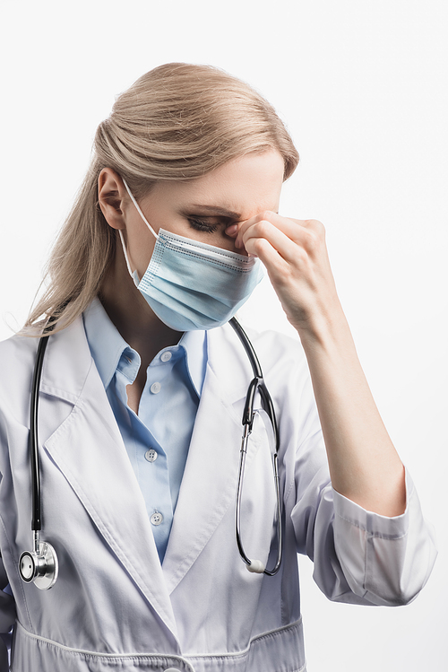 tired nurse in medical mask and white coat suffering from headache isolated on white