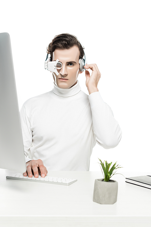 Cyborg in headphones and eye lens  near notebook, computer and plant on blurred foreground isolated on white