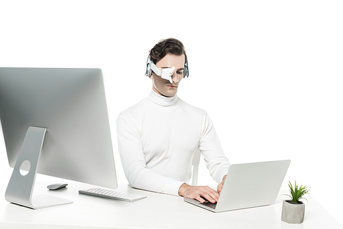 Cyborg in eye lens and headphones using laptop near computer and plant on blurred foreground isolated on white