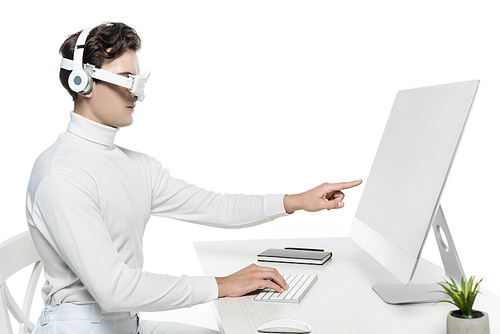 Cyborg in headphones and eye lens pointing at computer near notebook and plant on blurred foreground isolated on white