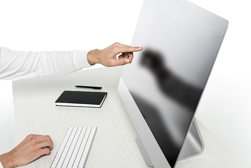 Cropped view of man pointing at computer with blank screen near notebook and pen on table isolated on white