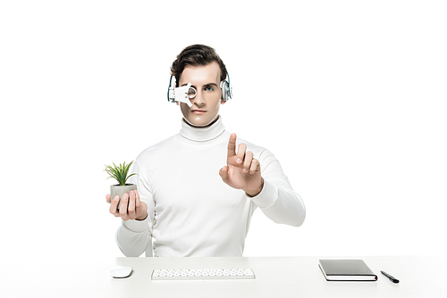 Cyborg in headphones holding plant and touching something near computer keyboard, mouse and notebook isolated on white