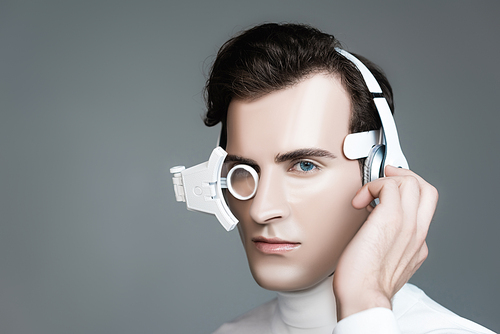 Cyborg man in digital eye lens adjusting headphones isolated on grey