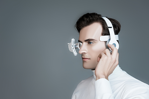 Cyborg in eye lens and headphones looking away isolated on grey