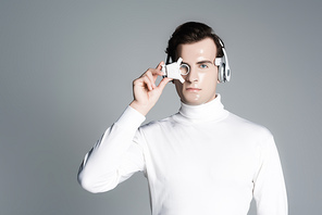 Cyborg in headphones holding digital eye lens isolated on grey