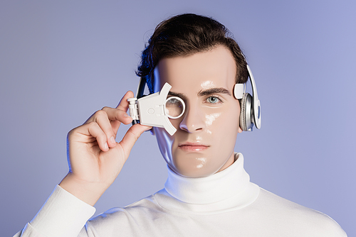 Cyborg man in headphones adjusting digital eye lens isolated on purple