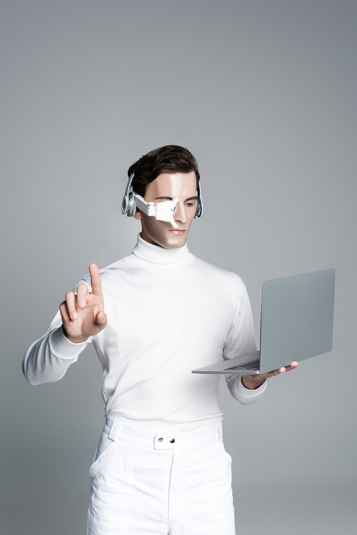 Cyborg man in headphones using laptop and touching something isolated on grey